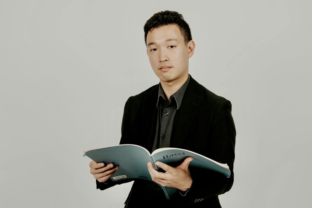 A musician in formal attire holding a music score book, looking confident.